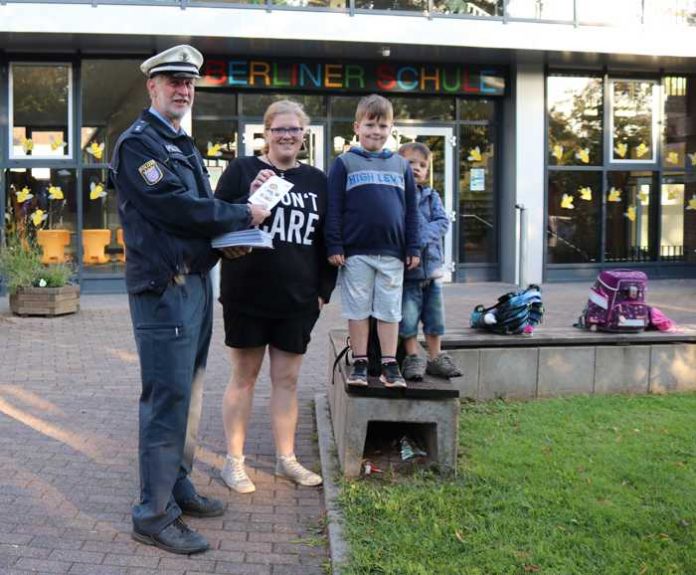 Uwe Maier von der Jugendverkehrsschule übergibt einer Mutter, die ihre beiden Kinder zur Schule bringt, einen Flyer vom Kinderkommissar LEON